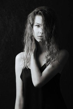 Dvushka ileriye bakıyor, elini omzuna kaldırıyor, kayışlara bir elbise takıyor, çıplak omuzlar, yüzünü kaplayan ıslak kıvırcık saçlar, siyah beyaz bir fotoğraf.,