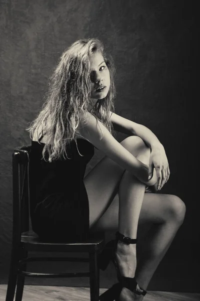 濡れた巻き毛の美しい女の子が椅子の上で曲げ曲げられストラップに小さな黒いドレス裸の肩と美しい肌長い脚 — ストック写真