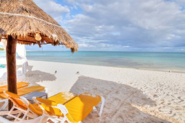 Hindistan cevizi palmiyeli saman plaj şemsiyesi ve beyaz kumlu sahildeki şezlonglar Riviera Maya, Cancun, Meksika.