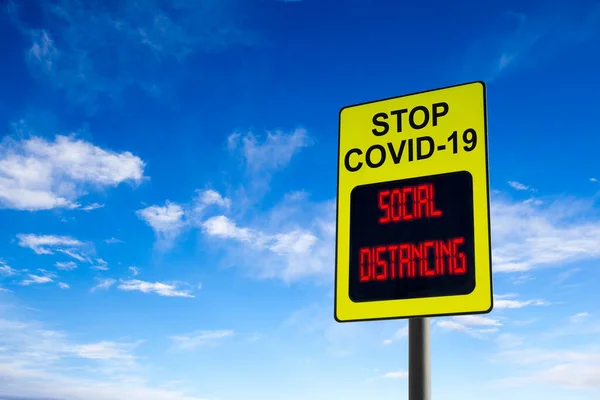A Stop COVID-19 sign with glowing digital message on social distancing and with copy space against blue sky. Concept of preventing the spread of the coronavirus pandemic.