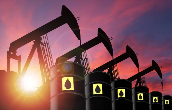 Rows of pump jacks silhouette and oil barrel drums against a sunset sky with deliberate lens flare and copy space. These jacks can extract between 5 to 40 litres of crude oil and water emulsion at each stroke.