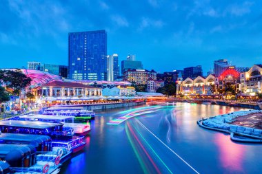 Singapur Nehri 'ndeki Clarke Quay rıhtımında gün batımında nehir teknelerinden ve çevresindeki barlardan ve restoranlardan gelen renkli ışık yolları sömürge döneminde ticari depo olarak kullanılan popüler turistik alanı aydınlatıyor..