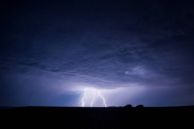 Ön planda iki arabanın siluetleriyle ovanın üzerinde şimşek çakıyor.