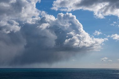Denizin üzerinde güneş tarafından aydınlatılmış kara bir yağmur bulutu.