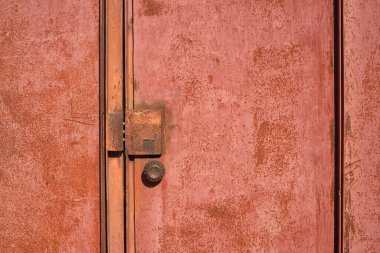 Paslı kırmızı metal bir kapının parçası. Kilidi kapalı ve sapı yuvarlak.