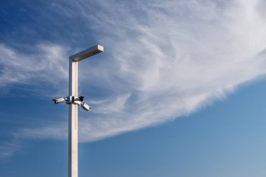 Mavi gökyüzü ve beyaz bulutlu bir fener direğinde üç video kamera.