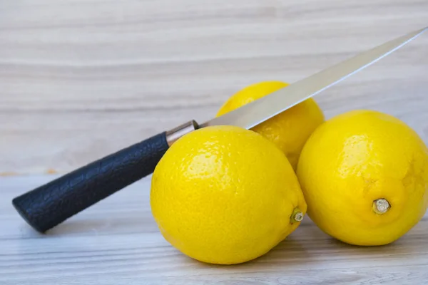 Tres limones jugosos con un cuchillo sobre un fondo de madera — Foto de Stock