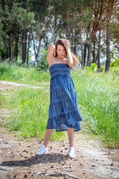 穿着蓝色衣服的年轻女子走在夏日的森林小径上 — 图库照片
