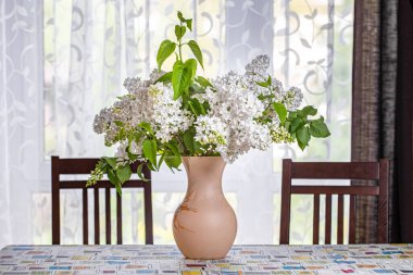 Mutfakta, pencerenin önündeki yemek masasındaki leylak buketi.