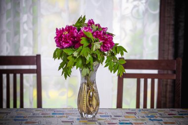 Mutfakta, pencerenin önündeki yemek masasındaki şakayık buketi.