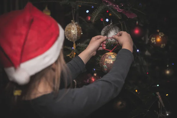 Mädchen Mit Weihnachtsmütze Schmückt Weihnachtsbaum Hause lizenzfreie Stockfotos