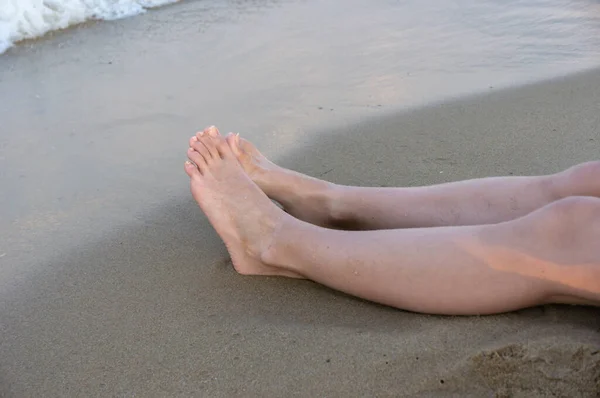 Girls\' feet on the sand. Near the surf line.