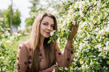 Güzel kız çiçek bahçesindeki beyaz çiçekleri kokluyor ve bize bakıyor.