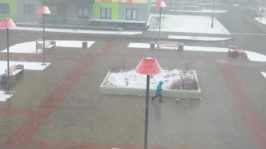 Bahçede yalnız başına sıcak kıyafetler giymiş bir çocuk futbol topuyla koşuyor. Islak bir sokakta koşmak. Karda çiçek tarhları. Kar yağıyor. Çevrelerinde renkli evler ve fenerler vardır..