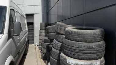 Eski yaz ve kış lastikleri, geri dönüşüm ve geri dönüşüm için birbiri üzerine katlanmış olarak duvarın önünde duruyor. Onları alıp götürecek bir makine var.