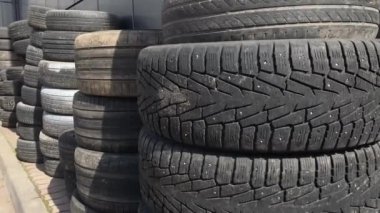 Eski yaz ve kış lastiklerinin kuleleri atılmak ve geri dönüşüm için üst üste yığılmış gri bir duvara karşı dururlar. Temizler ve güneş üzerlerinde parlıyor.