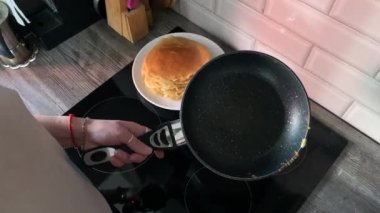 Kadın elleri fırından kızartma tavasını kaldırır ve bitmiş krepini mutfaktaki bir yığın gözlemenin üzerine atar. Yeni bir gözleme pişirmek için hamuru kaşığa döker.