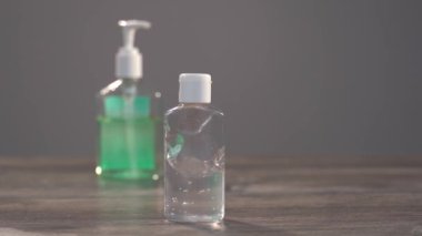Masanın üzerinde farklı boyutlarda iki jel antiseptik dezenfektan duruyor. Plastik şişelerden birinin odak noktası, içinde şeker kutusu olan diğerine gidiyor. Kavanozda el dezenfektanında..