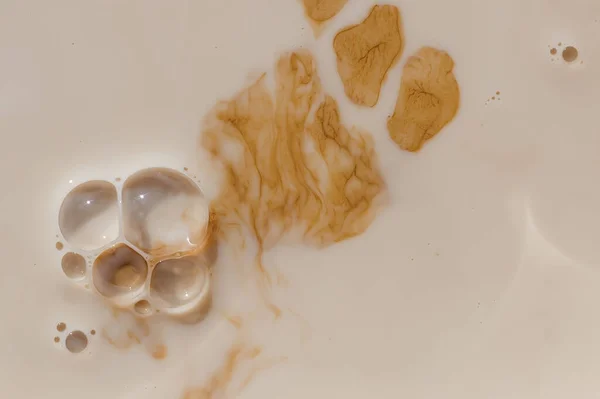 Brown stains in beige liquid with bubbles