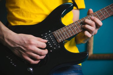 Erkek bir elektro gitar dizeleri eller. Siyah gitar closeup oynarken.