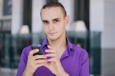 Mor bir gömlek yakışıklı, genç bir adam telefonda konuşuyor. Bir alışveriş merkezinde bir adam elinde bir cep telefonu ile modeli