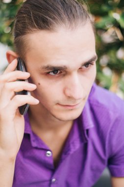 Mor bir gömlek yakışıklı, genç bir adam telefonda konuşuyor. Bir alışveriş merkezinde bir adam elinde bir cep telefonu ile modeli