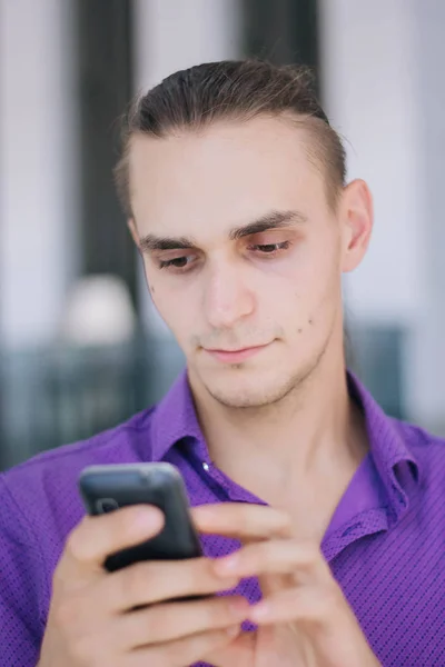 보라색 셔츠에 잘생긴 남자는 전화에 이야기입니다 손에서 휴대폰 쇼핑몰에서 — 스톡 사진