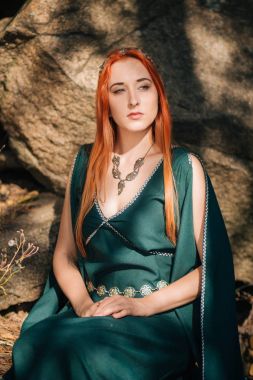 Turkuaz elbise ve bir diadem başında güzel bir kızıl saçlı kız sonbahar ormanda yürüyor. Bir elf görüntüde. Bu dağlarda büyük kayalar. Güneş parlamayı. Fantezi