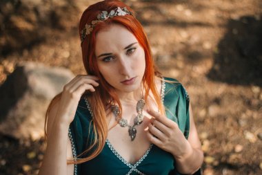 Turkuaz elbise ve bir diadem başında güzel bir kızıl saçlı kız sonbahar ormanda yürüyor. Bir elf görüntüde. Bu dağlarda büyük kayalar. Güneş parlamayı. Fantezi