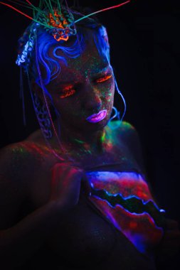 Neon kız portresi. Parlak yüzünde sıçramalarına. Koyu mavi neon lensler ile model. Cadılar Bayramı için görüntü.