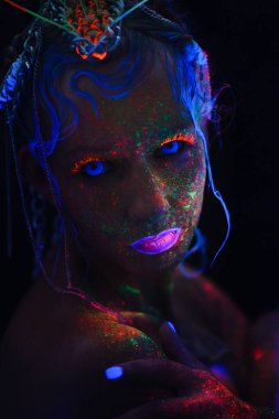Neon kız portresi. Parlak yüzünde sıçramalarına. Koyu mavi neon lensler ile model. Cadılar Bayramı için görüntü.