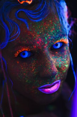 Neon kız portresi. Parlak yüzünde sıçramalarına. Koyu mavi neon lensler ile model. Cadılar Bayramı için görüntü.