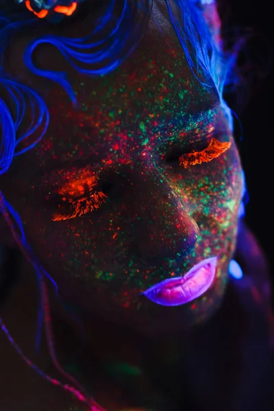 Neon portrait of a girl. Bright splashes on the face. Model with blue neon lenses in the dark. The image for halloween.