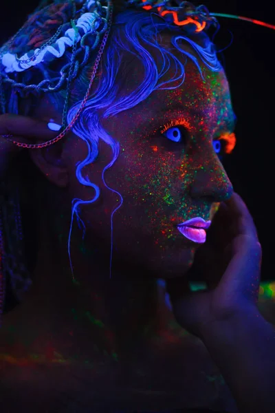 Neon portrait of a girl. Bright splashes on the face. Model with blue neon lenses in the dark. The image for halloween.