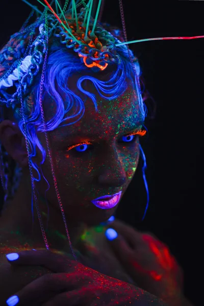 Neon kız portresi. Parlak yüzünde sıçramalarına. Koyu mavi neon lensler ile model. Cadılar Bayramı için görüntü.