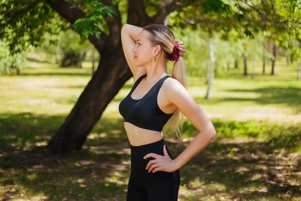 Beautiful girl in sportswear, black clothes playing sports outdoors in the park. — Stock Photo, Image