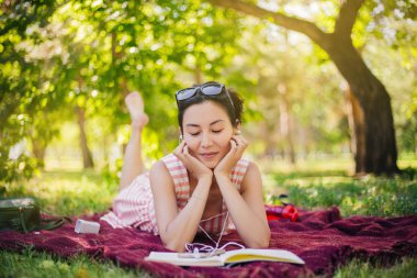 Kız çimlere uzanıyor ve bir not defterinden dersler okuyor. Bir kadın bir kitap okuyor ve parkta müzik dinliyor. Açık hava eğitimi