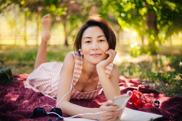 The girl lies on the grass and reads lectures in a notebook. A woman reads a book and listens to music in the park. Outdoor education