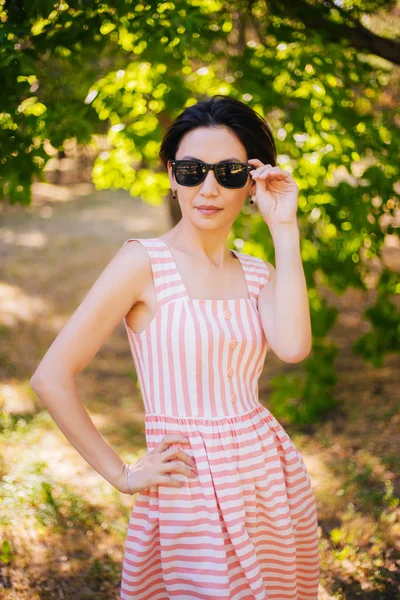 Meisje in een gestreepte jurk en zonnebril in het park. Wandelen in de natuur — Stockfoto