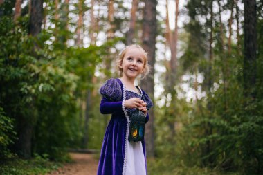 Mor ortaçağ elbisesi içinde beyaz saçlı küçük bir kız elinde lambayla duruyor. Peri prensesi karanlık ormanda kayboldu..