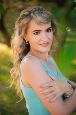 Parkta yürüyüş yapan güzel bir kız. Ormandaki mavi tişörtlü sarışın. Neşeli bir gülümsemesi olan manken.