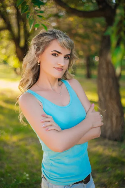 Beautiful girl on a walk in the park. Blonde in a blue t-shirt in the forest. Model with a cheerful smile — Stock Photo, Image