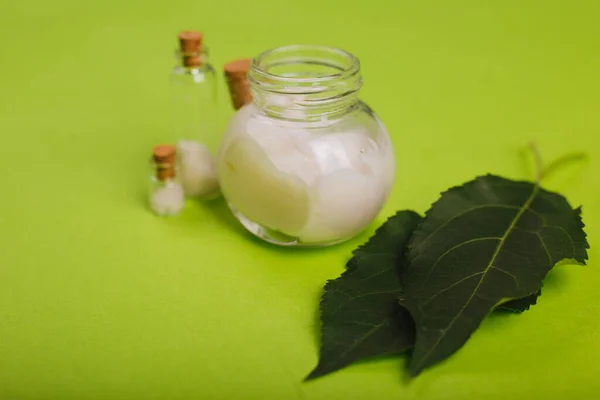 Eco cosmetics. A jar of white cream and the leaves of the tree on a green background. Skin care. Sea salt jars