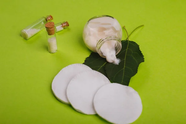 Eco cosmetics. A jar of white cream and the leaves of the tree on a green background. Skin care. Sea salt jars