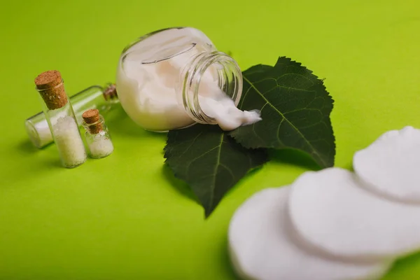 Eco cosmetics. A jar of white cream and the leaves of the tree on a green background. Skin care. Sea salt jars