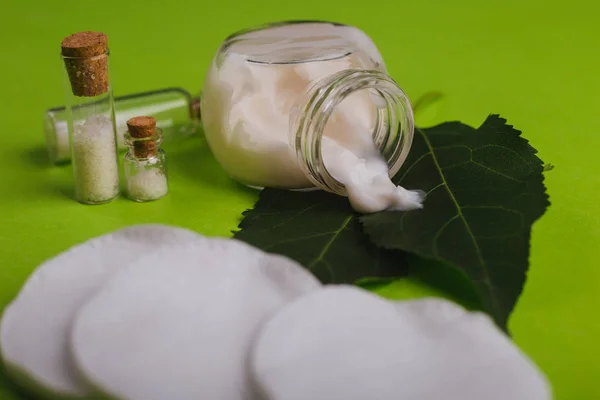 Eco cosmetics. A jar of white cream and the leaves of the tree on a green background. Skin care. Sea salt jars