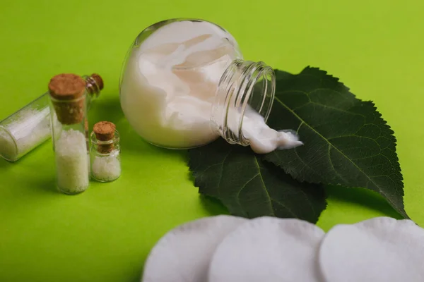 Eco cosmetics. A jar of white cream and the leaves of the tree on a green background. Skin care. Sea salt jars