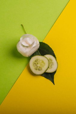 Sarı-yeşil arka planda beyaz salatalık kremi. Yapraklar ve taze salatalıkla