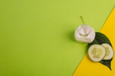 Sarı-yeşil arka planda beyaz salatalık kremi. Yapraklar ve taze salatalıkla