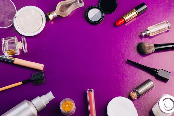 Scattered cosmetics on a purple background. The contents of women\'s handbags. Lady set. Lipstick, perfume and shadow. View from above